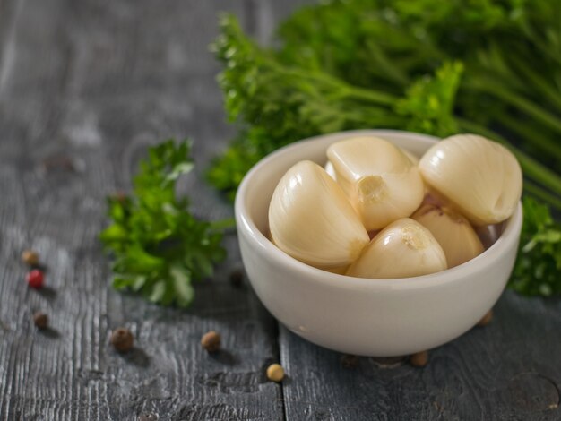 Peeled garlic cloves in a porcelain Cup with parsley leaves on a wooden table