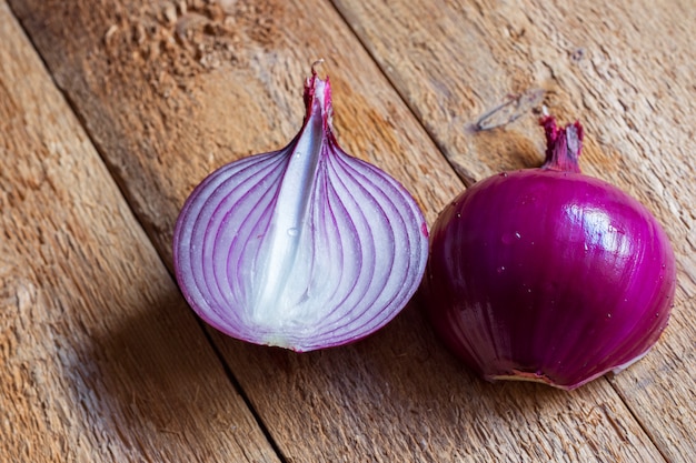 Bulbo sbucciato diviso in due della cipolla rossa con le gocce di acqua sulla tavola di legno stagionata