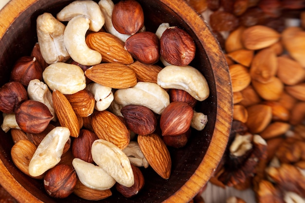 Peeled  hazelnut, cashew, almond  in a wooden cedar plate on the background a scattering of various nuts. Peeled hazelnut, cashew