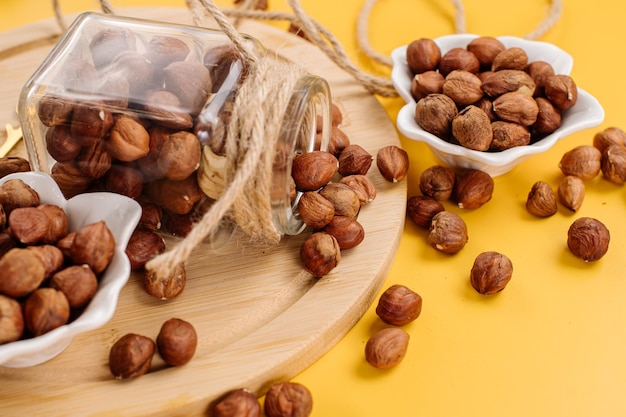 Peeled hazelnuts in a bowl and also scattered on a yellow background