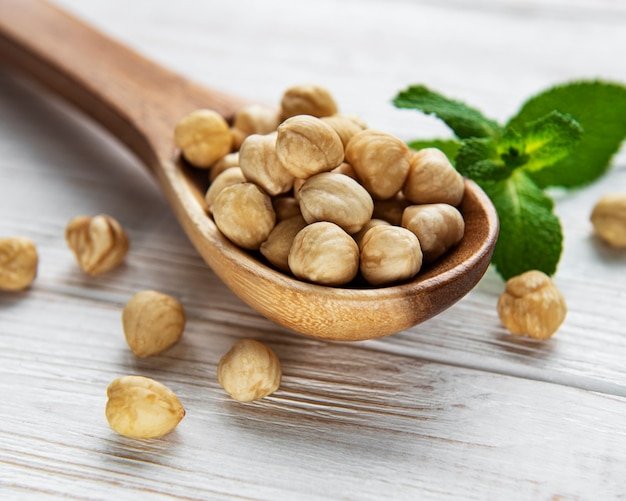 Peeled hazelnuts in a spoon on white wooden background