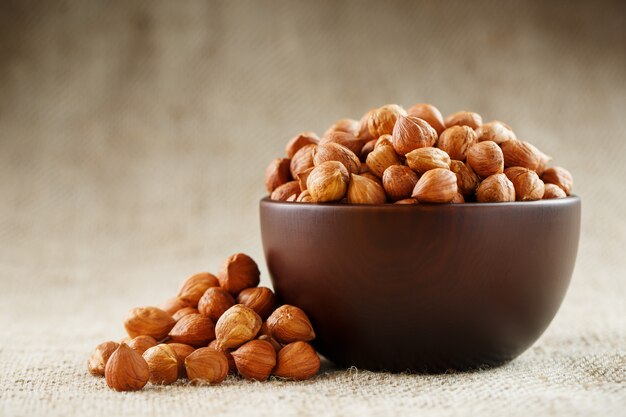 Peeled hazelnuts in a wooden, dark brown cup on a burlap cloth