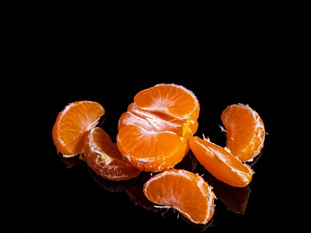 Peeled mandarin fruit slices on a black background