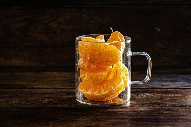 Peeled mandarin slices in a glass on a wooden background.