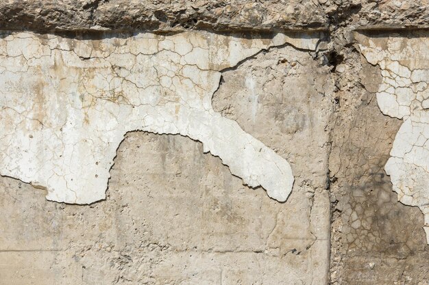 Peeled off plaster on distressed concrete wall under direct sun light