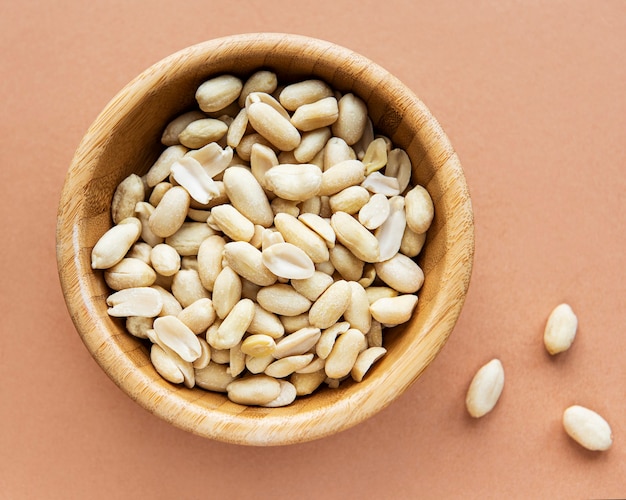 Peeled peanuts in a wooden bowl on a brown background