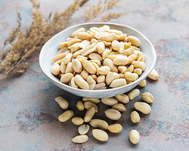 Peeled peanuts in a wooden bowl on a grey concrete surface