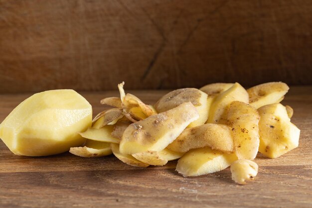 A peeled potato and pile of potatoes peel or skin on wood