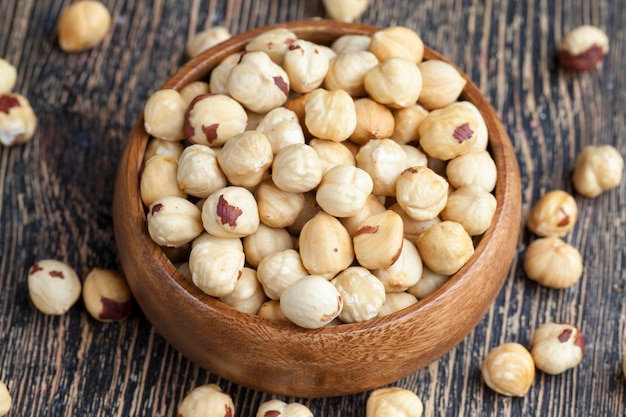 Peeled and roasted hazelnuts in a wooden bowl and on a wooden table, close-up of healthy roasted hazelnuts