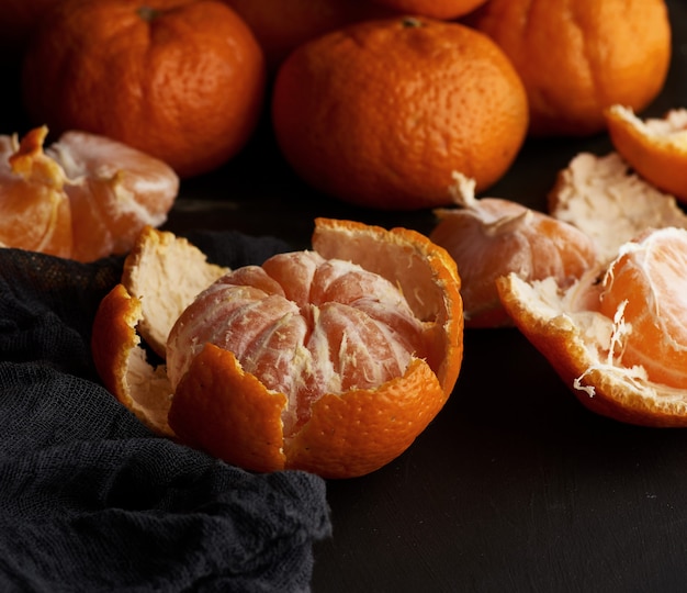 Peeled round ripe tangerines in a plate on a black textile napkin