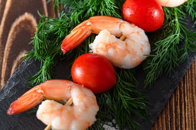 Photo peeled shrimps and red tomato on a wooden stick and dill closeup