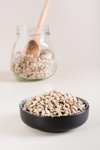 Peeled sunflower seeds in a bowl and in a glass jar on the table Organic food Vertical view