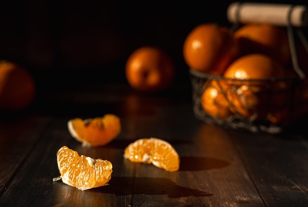 peeled tangerine slices in harsh light in the foreground and several tangerines in a basket in the b
