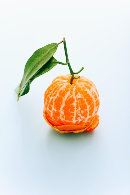 Peeled tangerine with leaves on light background