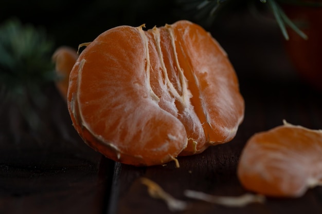 A peeled tangerine on a wooden table among spruce twigs