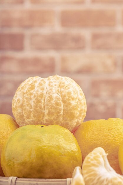 Photo peeled tangerines in a bamboo sieve basket on dark wooden table with red brick wall background chinese lunar new year fruit design concept close up