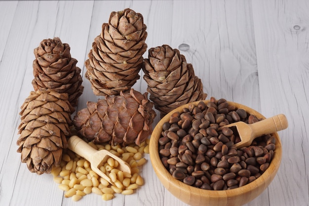 Peeled and unrefined pine nuts and cedar cones on a wooden table.