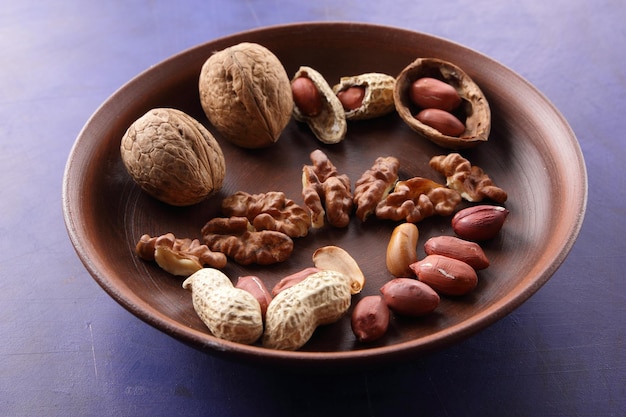 Peeled and unshelled nuts on a blue background closeup Walnuts and peanuts on a clay plate on a bluee background Vegan food