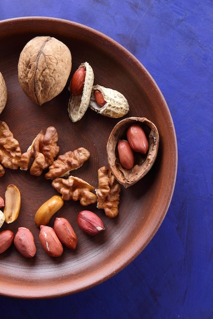 Peeled and unshelled nuts on a blue background closeup Walnuts and peanuts on a clay plate on a bluee background Vegan food