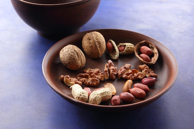 Peeled and unshelled nuts on a blue background closeup Walnuts and peanuts on a clay plate on a bluee background Vegan food