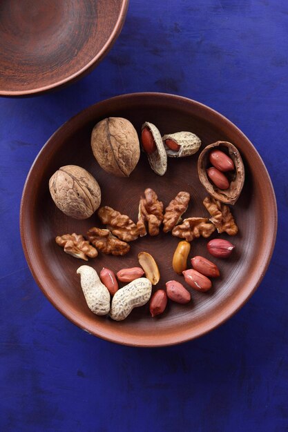 Peeled and unshelled nuts on a blue background closeup Walnuts and peanuts on a clay plate on a bluee background Vegan food