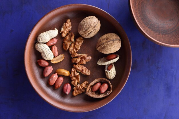 Peeled and unshelled nuts on a blue background closeup Walnuts and peanuts on a clay plate on a bluee background Vegan food