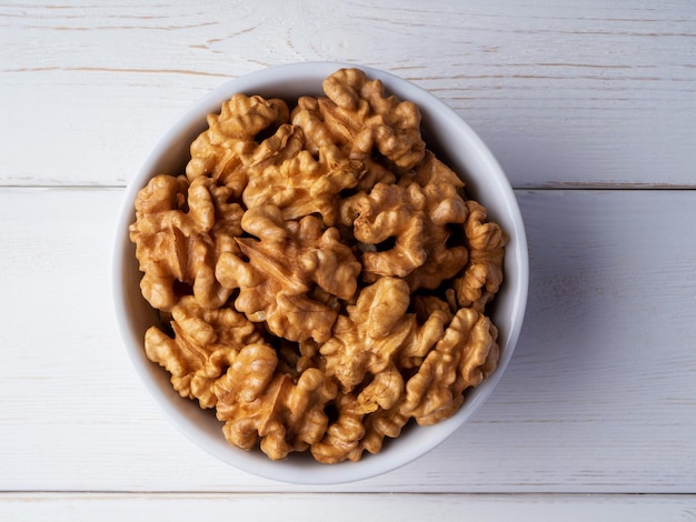 Peeled walnuts in a bowl on a white wooden background Closeup