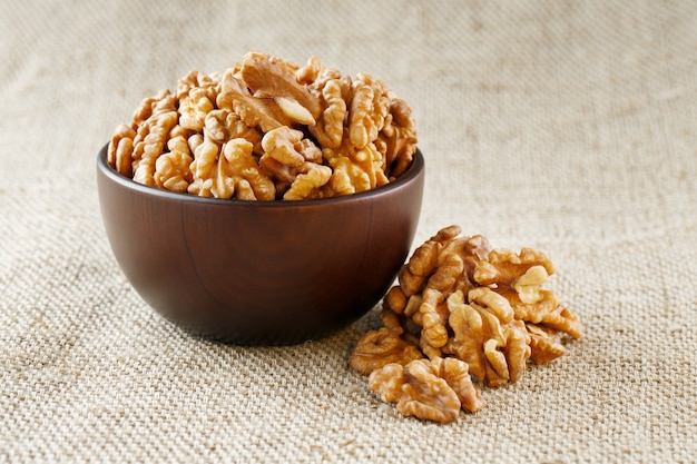 Peeled walnuts in a wooden, dark brown cup on a burlap cloth