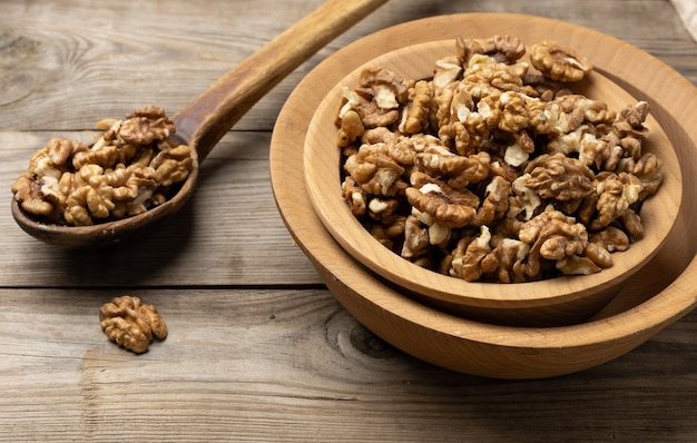 Peeled walnuts in a wooden plate on the table, top view