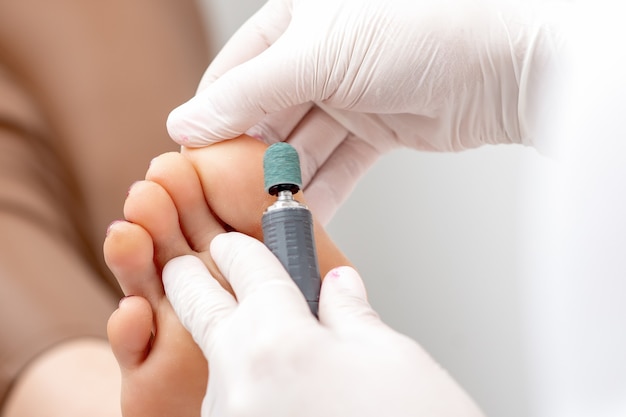 Peeling feet pedicure procedure from callus on foot by hands of podiatrist in white gloves at beauty salon