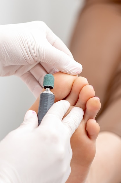 Peeling feet pedicure procedure from callus on foot by hands of podiatrist in white gloves at beauty salon