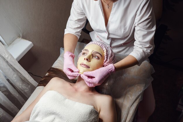 Maschera peeling all'oro per una bella pelle del viso. cosmetologo che fa la procedura di bellezza per il paziente