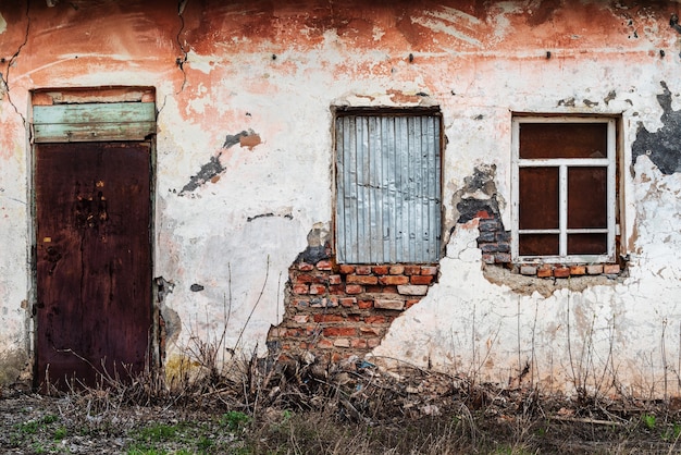 peeling wall of old abandoned building with closed doors and two windows Russia Orenburg region