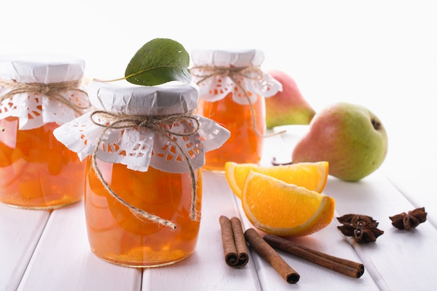 Peer en sinaasappeljam in glazen potten met rijpe peren, kaneelstokjes, anijs sterren en groene bladeren op tafel.