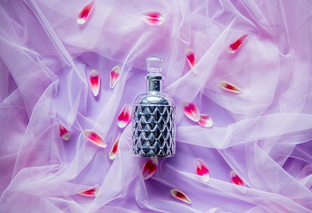 Photo pefume bottle in purple tulle on background with tulip petals