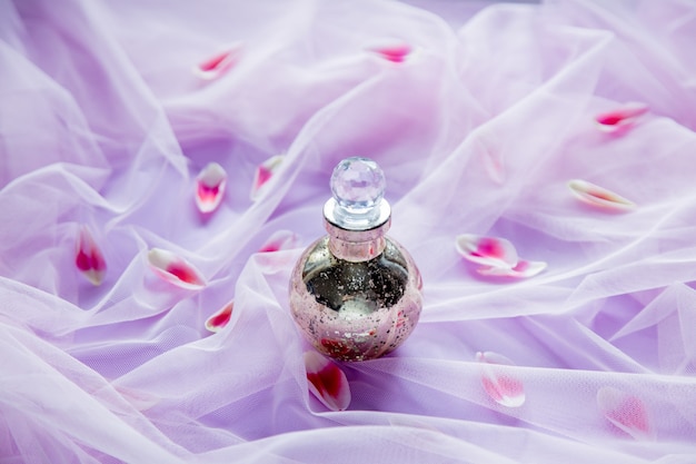 Photo pefume bottle in purple tulle on background with tulip petals