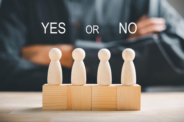 Foto le bambole peg su cubi di legno raffigurano le scelte sì o no la mano dell'uomo tiene due opzioni per la presa di decisioni il segno d'interrogazione rosso rafforza il concetto di pensare con la scelta sì o no