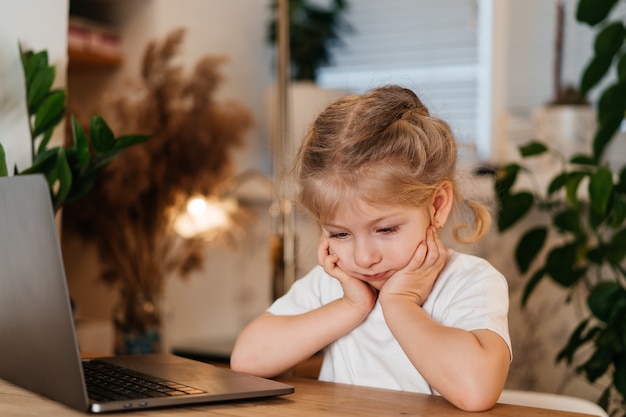 peinzend blond meisje zit achter een laptop met een droevig gezicht