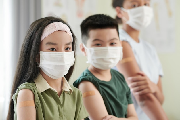 Peinzend meisje met medisch masker krijgt vaccin tegen coronavirus met haar klasgenoten