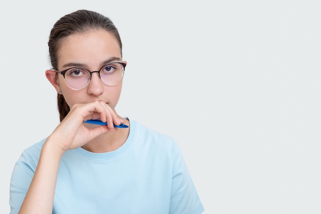 Peinzende aantrekkelijke studente die een pen in haar mond houdt en naar jou kijkt op een witte achtergrond met kopieerruimte. Moeilijke studie op de universiteit, instituutconcept.