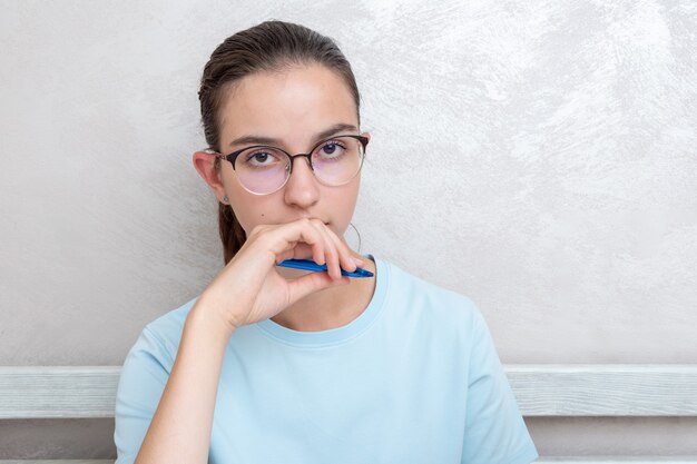 Peinzende aantrekkelijke vrouwelijke student die pen in de mond houdt en naar jou kijkt, kopieer ruimte. meisje student studeert thuis. terug naar schoolconcept. thuisonderwijs concept.