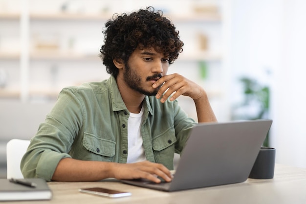 Peinzende donkerhuidige man zit aan het bureau voor laptop