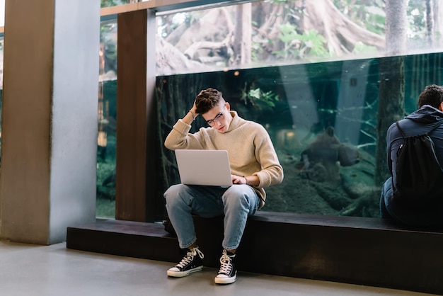 Peinzende hipstermens met laptop in gang