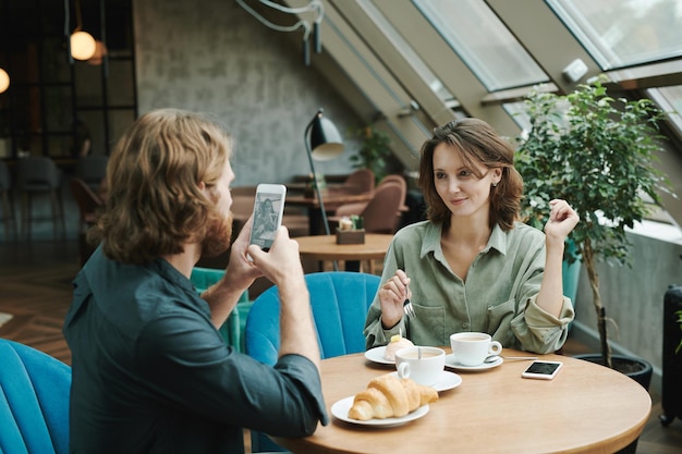 Peinzende jonge, bebaarde smm-manager die koffie drinkt en tijdens het werk aan het bericht van de klant denkt