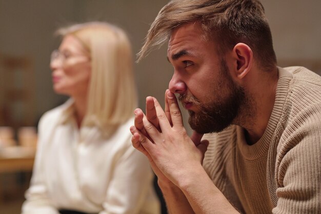 Foto peinzende jonge man die handen bij het gezicht houdt terwijl hij naar iemand luistert