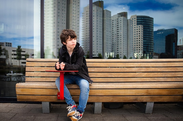 Peinzende jonge tiener jongen zittend op een bankje in de straat opzij kijkend Nederland Rotterdam