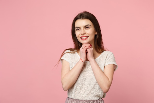 Peinzende jonge vrouw in casual lichte kleding poseren geïsoleerd op pastel roze muur achtergrond, studio portret. mensen levensstijl concept. bespotten kopie ruimte. leg de handen op de kin en kijk opzij.