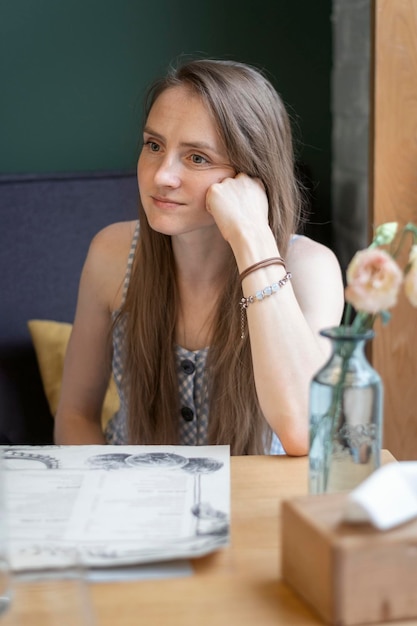 Peinzende jonge vrouw zit in een café met haar hoofd op haar hand Vermoeide blik naar nergens