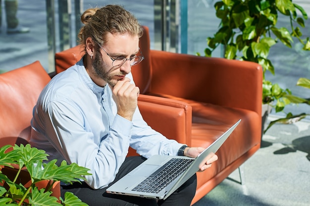 Peinzende jonge zakenman werkt op een laptop, in een modern kantoor.