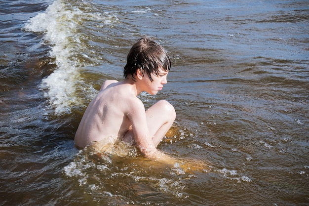 Peinzende jongen zit in de branding tussen de golven.